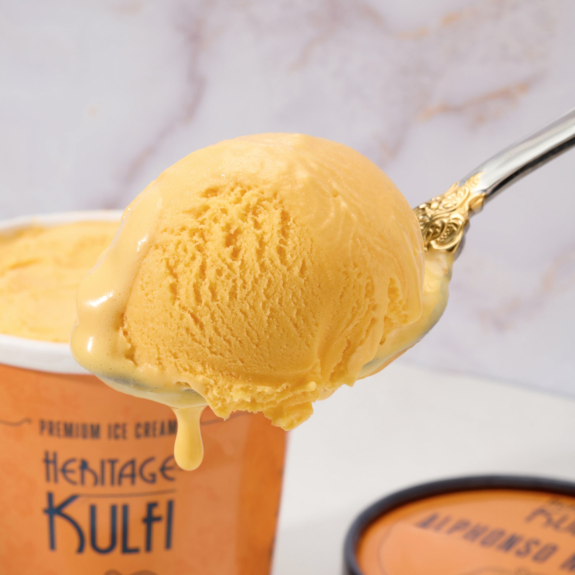 Closeup of a scoop of brightly colored mango kulfi as it drips from a silver spoon