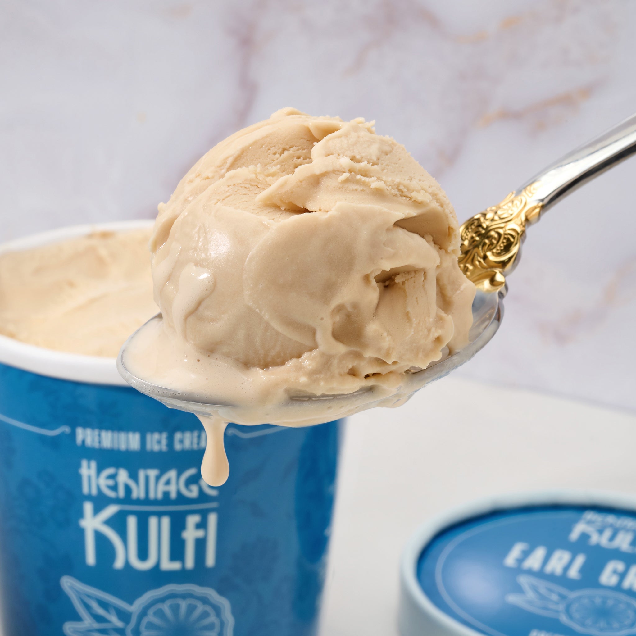A scoop of earl-grey colored kulfi drips from a silver spoon