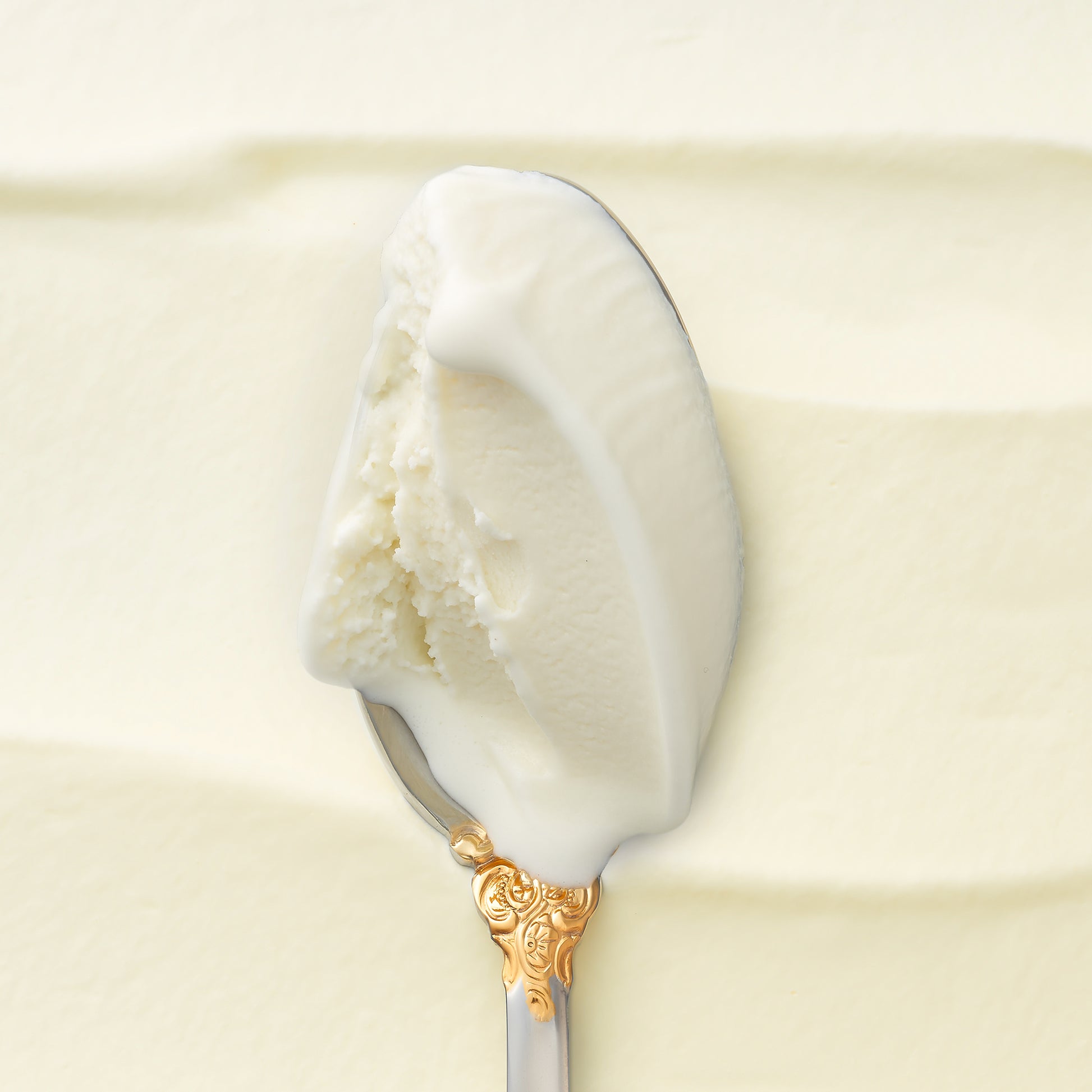 A closeup of a creamy scoop of kulfi on a silver spoon, with a cream swirled backdrop
