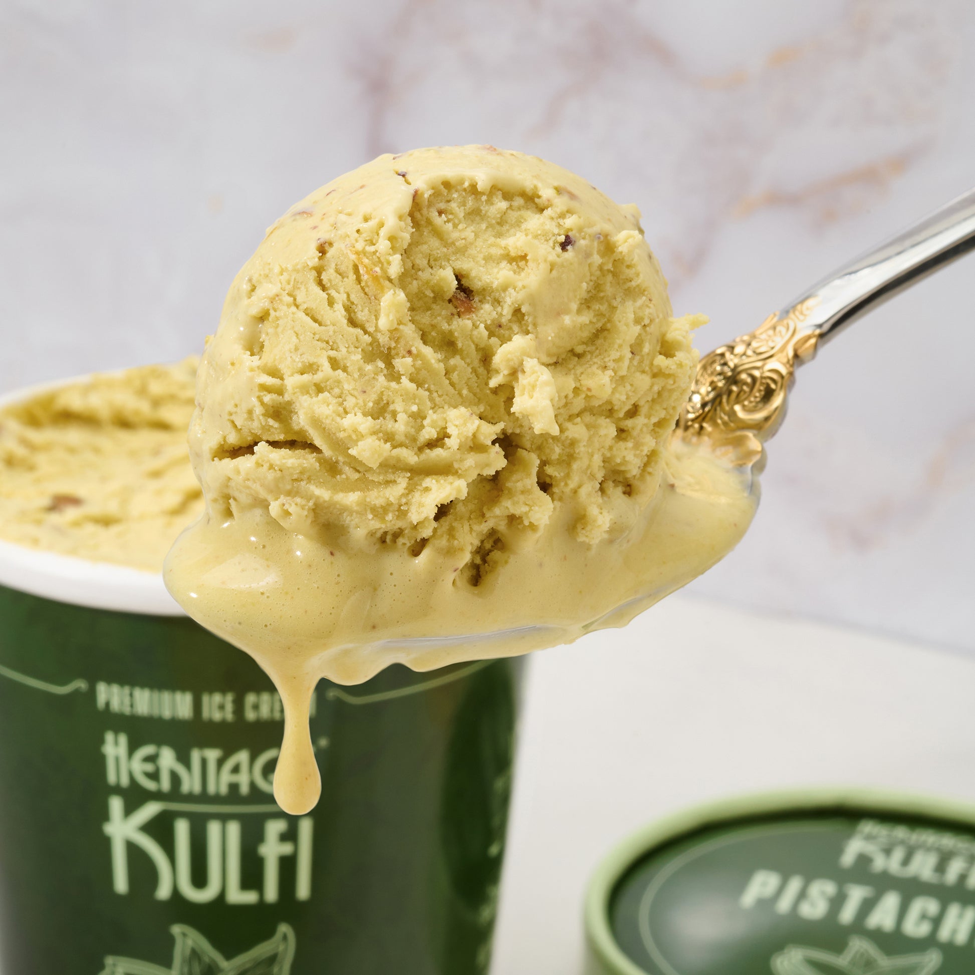 A closeup of a scoop of pistachio kulfi dripping from a silver spoon