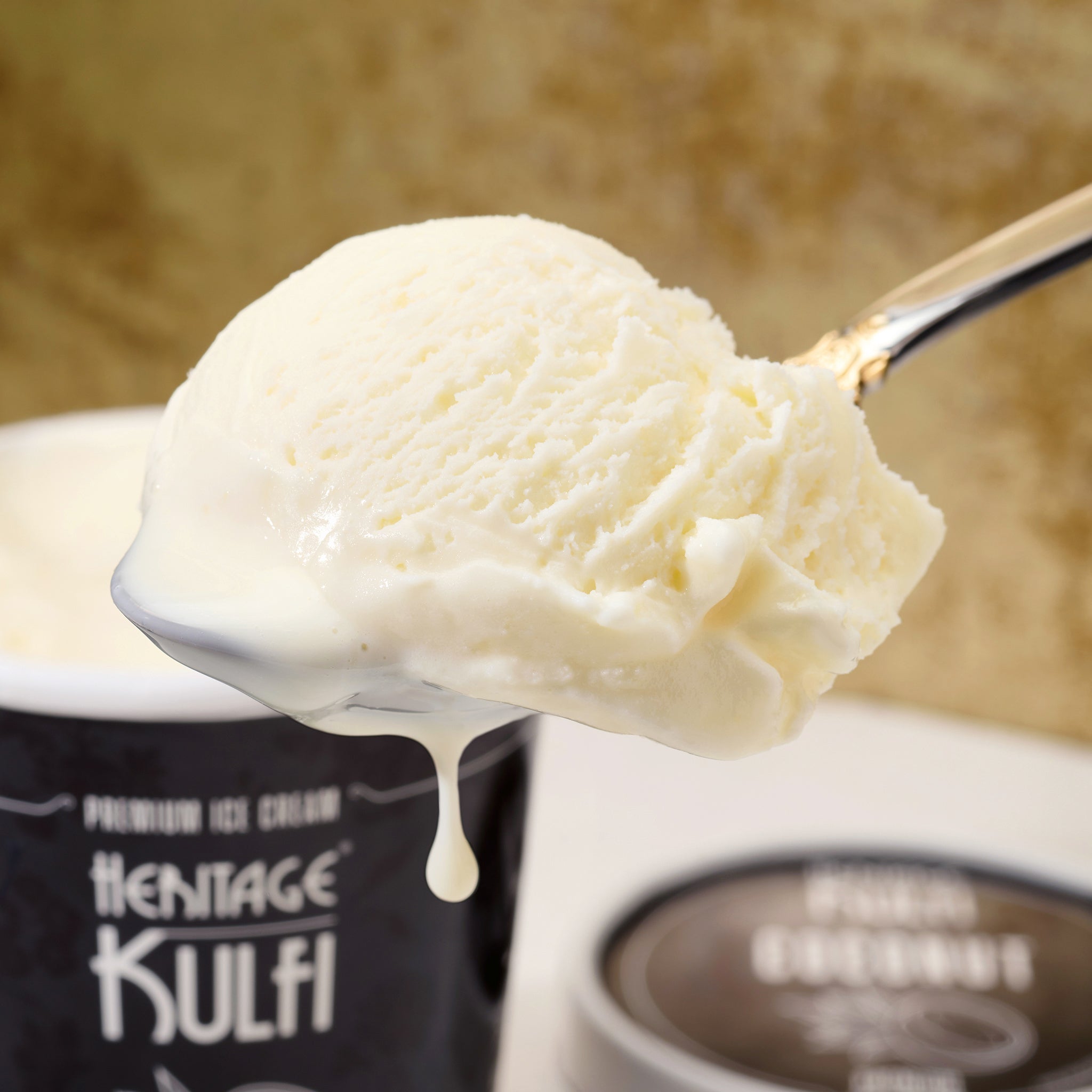 A scoop of coconut kulfi drips from a silver spoon