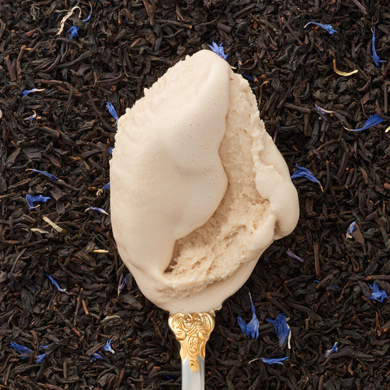 A closeup of a scoop of earl grey kulfi on a silver spoon, with a backdrop covered in earl grey tea leaves