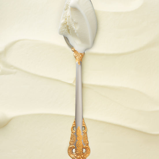 A scoop of malai sweet cream kulfi in a silver spoon with a gold handle, against a soft, creamy backdrop.