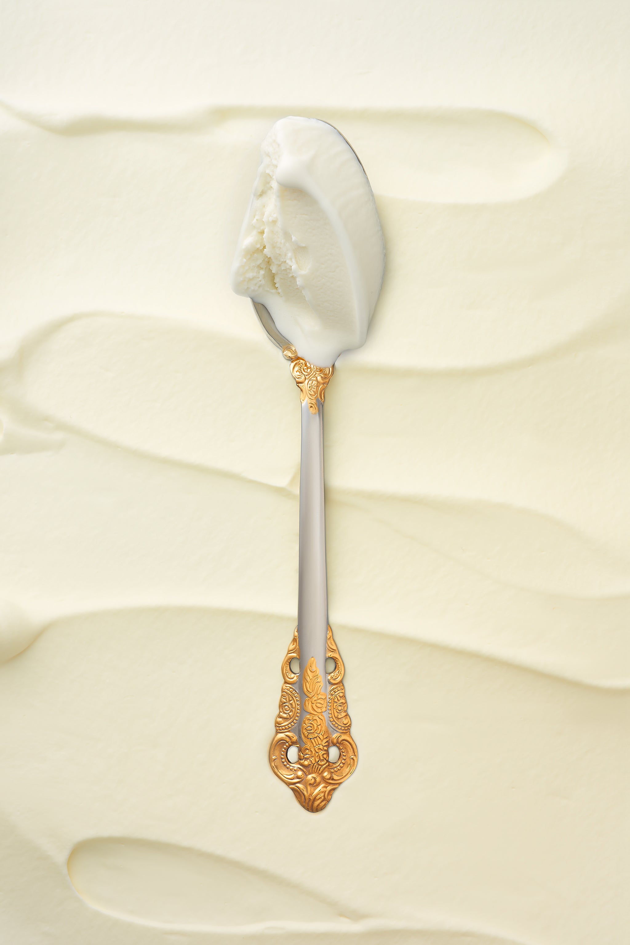 A scoop of malai sweet cream kulfi in a silver spoon with a gold handle, against a soft, creamy backdrop.