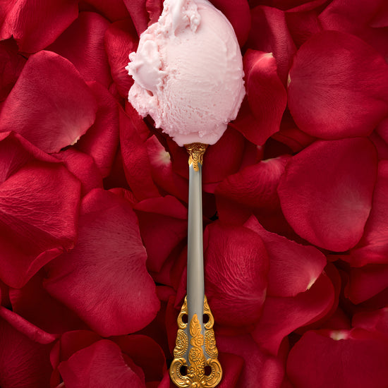Rosewater kulfi in a decorative spoon, with a soft focus backdrop of scattered rose petals.