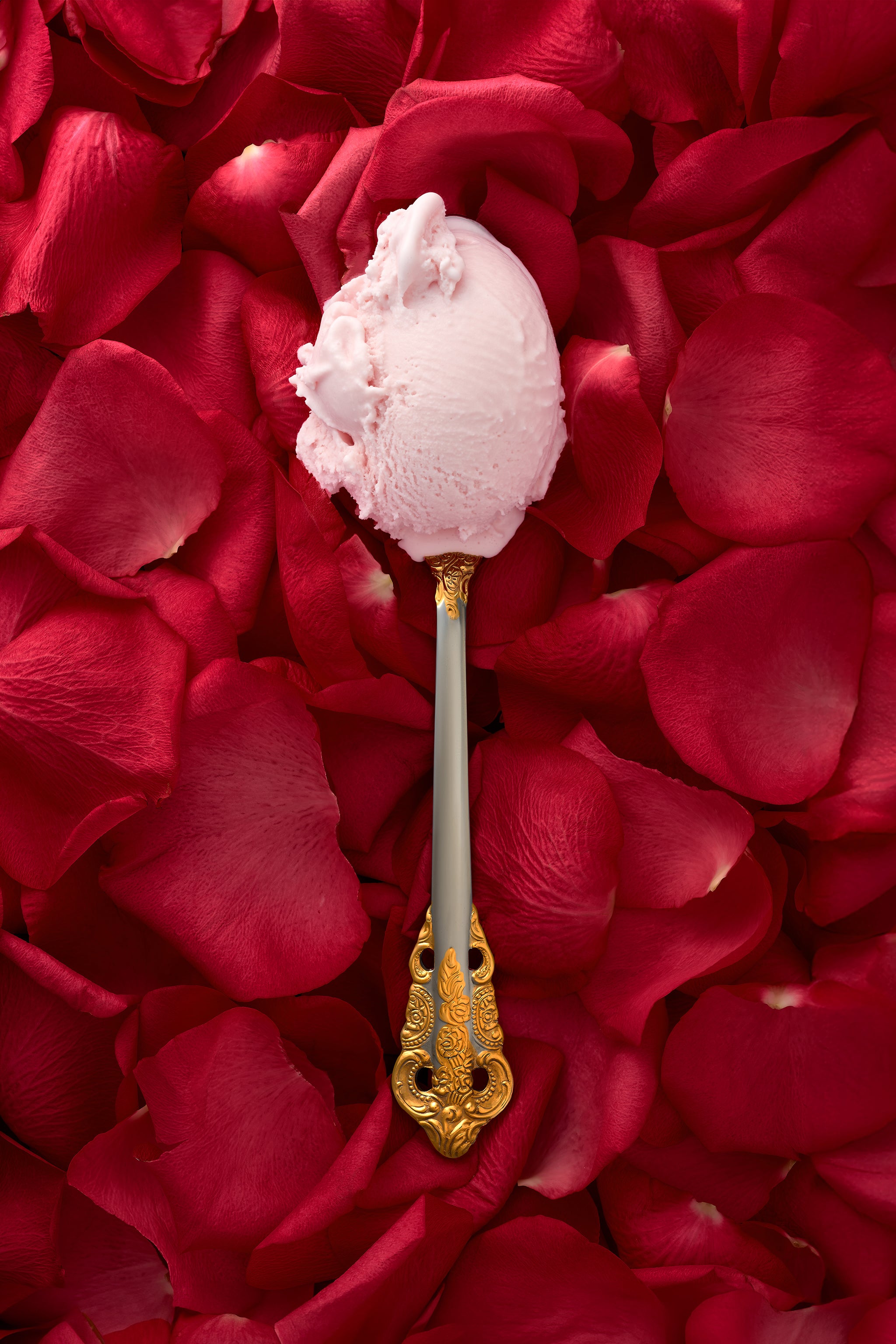 Rosewater kulfi in a decorative spoon, with a soft focus backdrop of scattered rose petals.